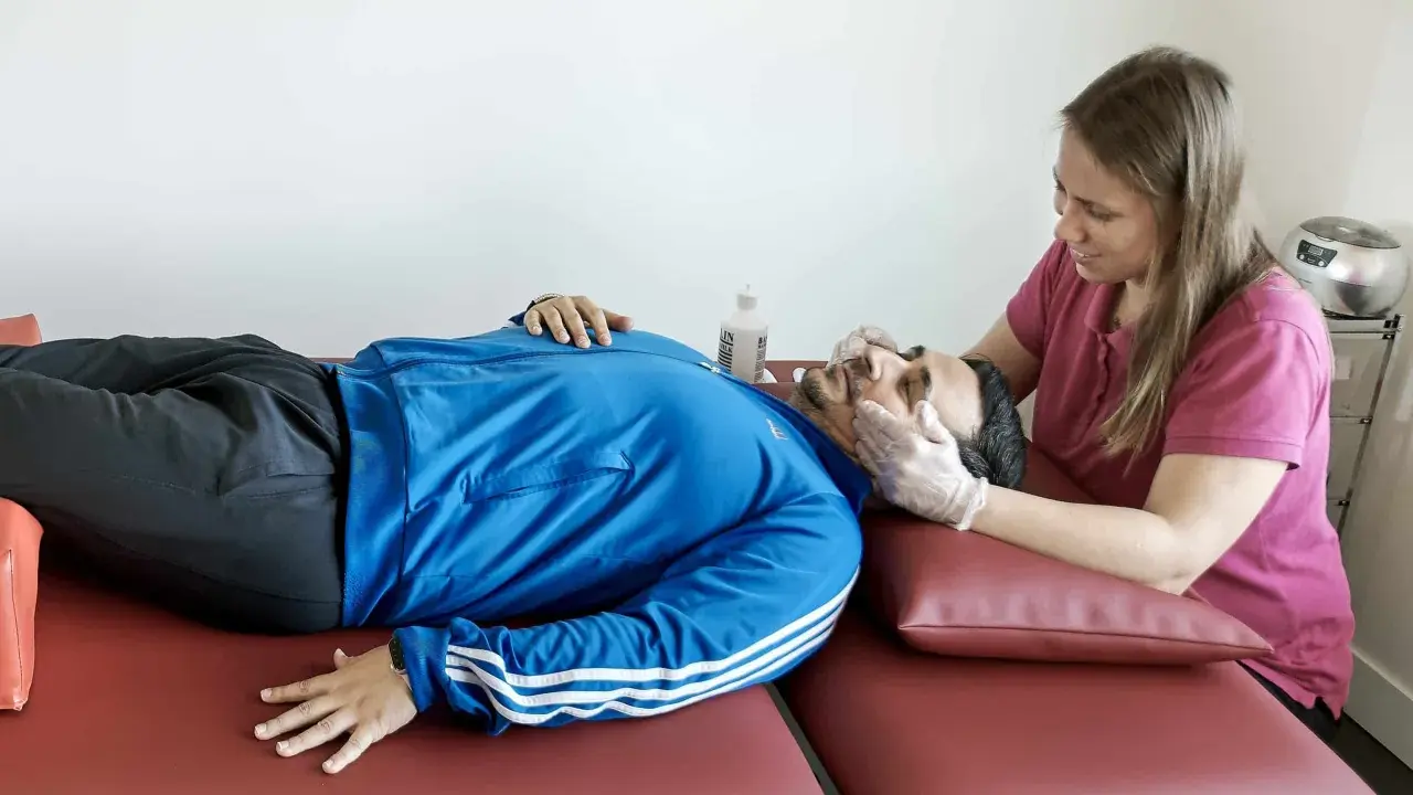 Fisioterapeuta evalúa la cabeza de un paciente con ataxia espinocerebelosa, buscando mejorar su equilibrio y coordinación.