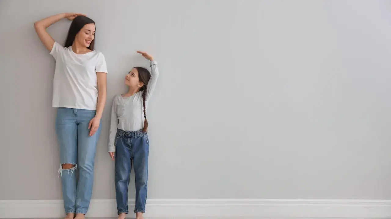 Madre e hija miden su altura. La estatura se hereda del padre o madre, y esta niña parece estar heredando la de su madre.