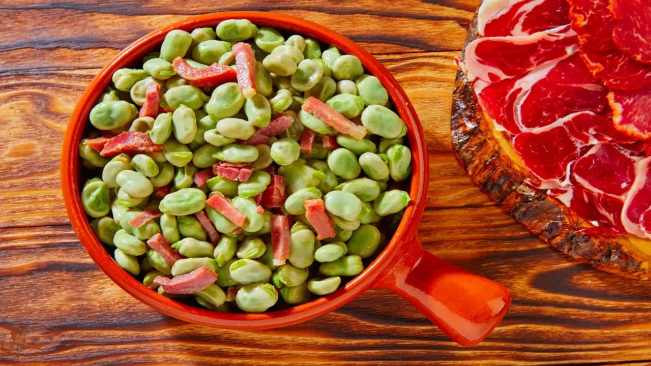 Un plato de habas tiernas con trocitos de jamón, ideal para quienes preguntan qué es el favismo y buscan recetas.