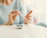 Mujer se pincha el dedo con un glucómetro. La diabetes es hereditaria, y el control es clave.