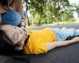 Niña inconsciente en el suelo, con una persona arrodillada a su lado, preocupada. Podría ser un síntoma de la enfermedad de Lafora.