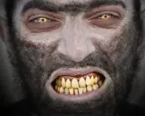 Rostro de hombre con ojos amarillos y colmillos afilados, cubierto de pelo oscuro. Parece sufrir la enfermedad del hombre lobo.