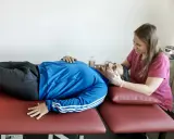 Fisioterapeuta evalúa la cabeza de un paciente con ataxia espinocerebelosa, buscando mejorar su equilibrio y coordinación.