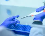 Manos con guantes azules manipulan tubos de ensayo y pipeta. Lydia Fairchild trabaja en el laboratorio, investigando con precisión.