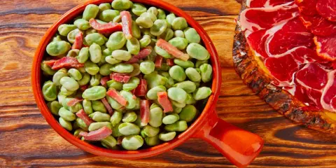 Un plato de habas tiernas con trocitos de jamón, ideal para quienes preguntan qué es el favismo y buscan recetas.