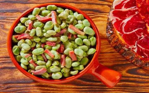 Un plato de habas tiernas con trocitos de jamón, ideal para quienes preguntan qué es el favismo y buscan recetas.