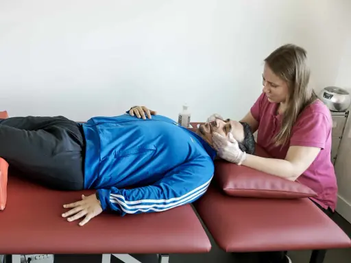 Fisioterapeuta evalúa la cabeza de un paciente con ataxia espinocerebelosa, buscando mejorar su equilibrio y coordinación.