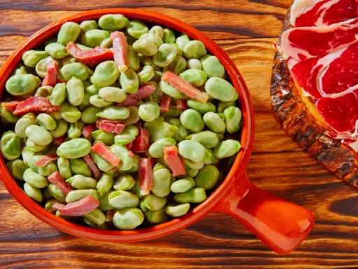 Un plato de habas tiernas con trocitos de jamón, ideal para quienes preguntan qué es el favismo y buscan recetas.