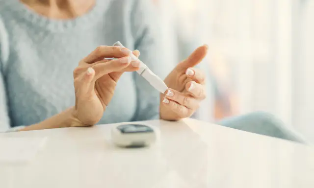 Mujer se pincha el dedo con un glucómetro. La diabetes es hereditaria, y el control es clave.
