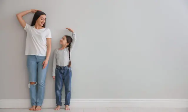 Madre e hija miden su altura. La estatura se hereda del padre o madre, y esta niña parece estar heredando la de su madre.
