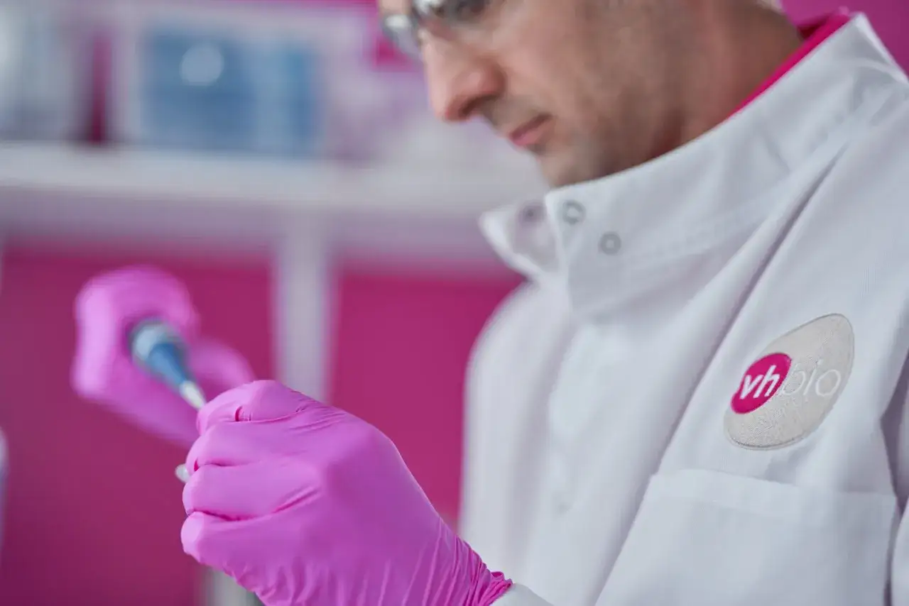 Cient&iacute;fico con guantes rosas manipula pipeta, investigando el quimerismo gen&eacute;tico en un laboratorio.